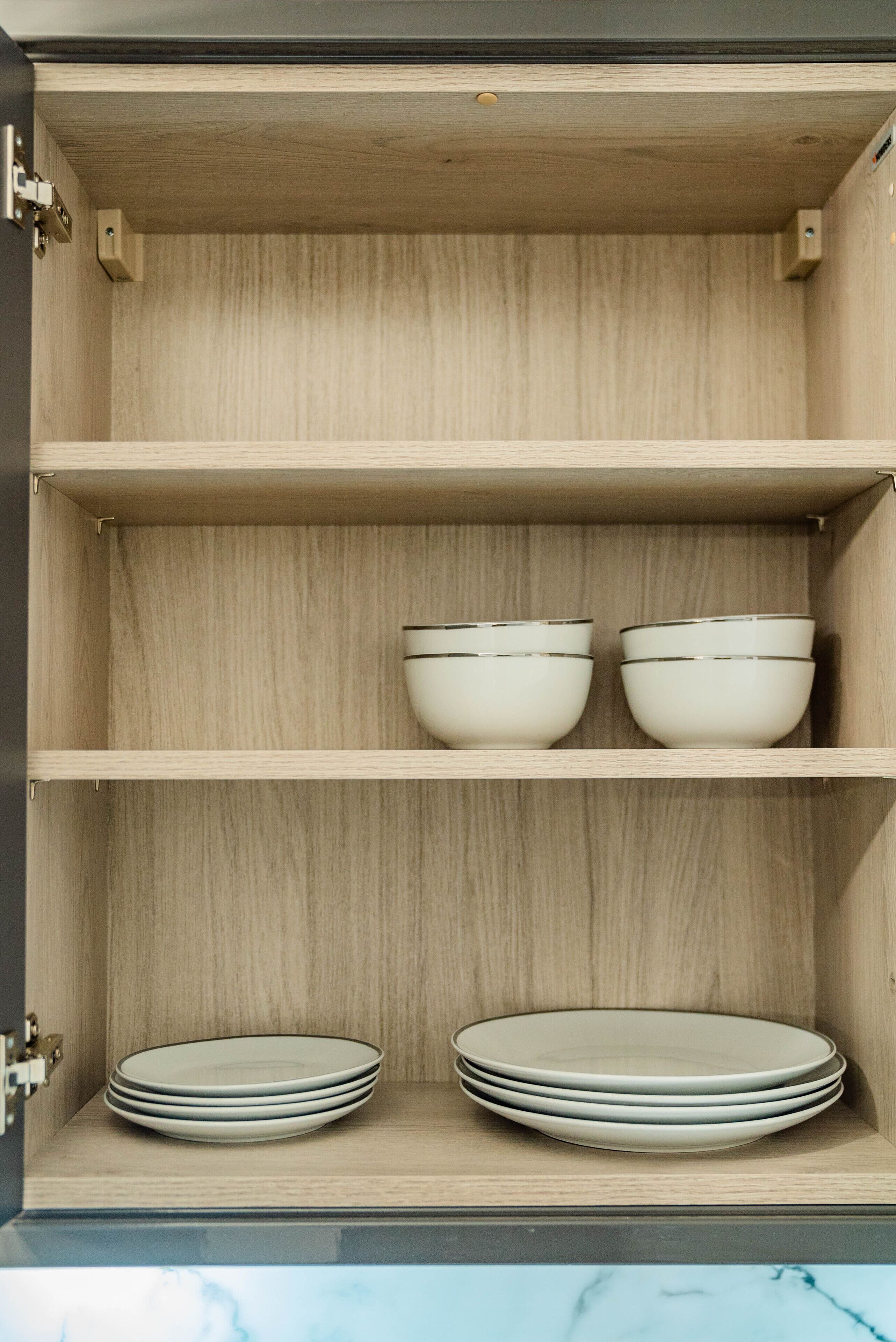 A wooden cabinet with two shelves; the top shelf holds two white bowls, and the bottom shelf holds a stack of white plates.