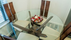 A glass-top dining table with four chairs, a bowl of assorted nuts and dried fruits, and a wooden accent wall. - TWO BEDROOM LUXURY GROUND FLOOR APARTMENT.  (London)