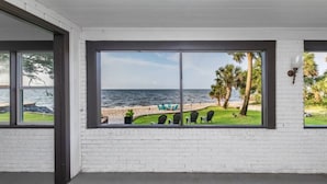 A room with large windows overlooking a beach, white brick walls, and a few outdoor chairs. - BAY HOUSE - Steps to its own Private Beach - Amazing Sunsets on the Water (Pensacola)