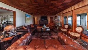 A spacious living room with a large leather sofa, a wooden ceiling, and a fireplace. - BAY HOUSE - Steps to its own Private Beach - Amazing Sunsets on the Water (Pensacola)