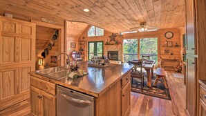 A wooden cabin with a kitchen featuring a large island, a dining area, and a fireplace. - Dreamy Ellijay Resort Cabin w/ Game Room & Decks! (Ellijay)