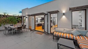 A modern outdoor patio with a dining area, a sofa with patterned cushions, and a view into the interior of the building. - StayCentral - Moonee Ponds Penthouse - Mount Alexander Rd, Moonee Ponds - 3 Bedrooms, 4 Beds, 2 Bathrooms, 2 secure undercover parking spot. (Moonee Ponds)