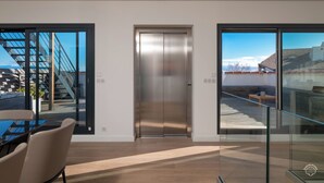 Et moderne interiør med en glas-trappe, en central elevator og et spiseområde med et bord og stole.