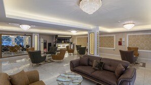 Un hall d’entrée spacieux, avec un canapé en cuir marron, une table basse ronde en marbre et un lustre.