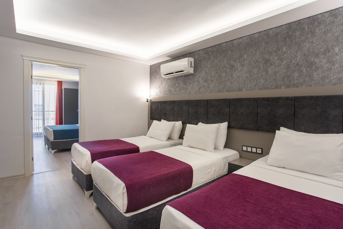 Een hotelkamer met drie bedden, een grijze structuurwand en een airconditioning.