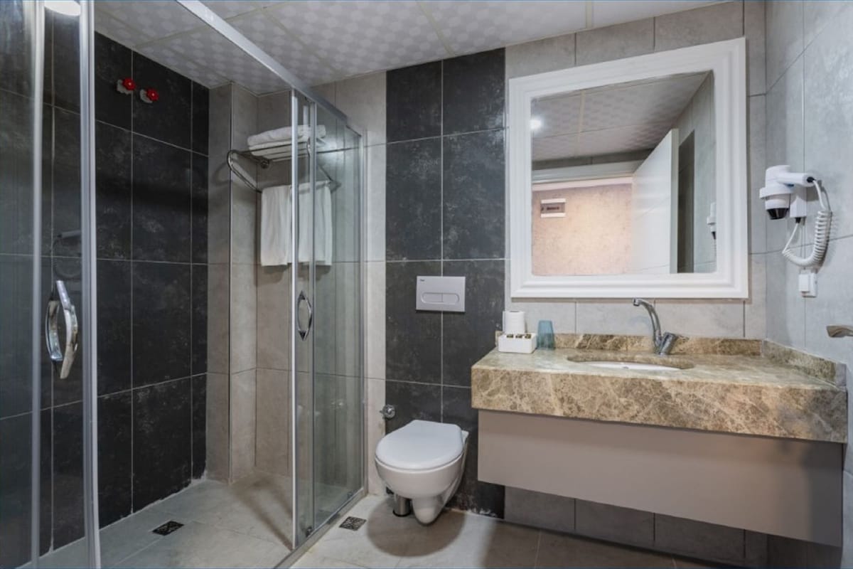 Een moderne badkamer met een douchecabine van glas, een wit toilet en een wastafel met een marmeren blad.