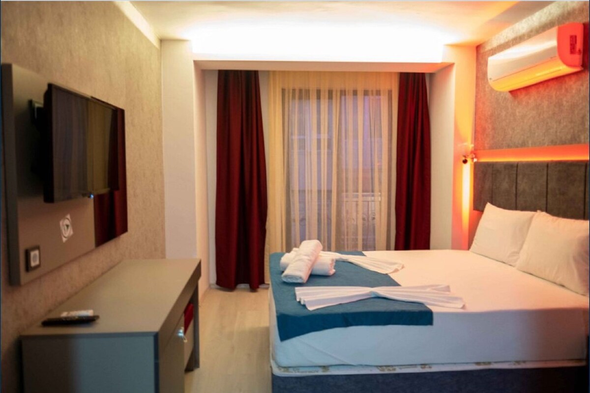 Une chambre d’hôtel avec un lit, une télévision, un bureau et une fenêtre avec des rideaux.