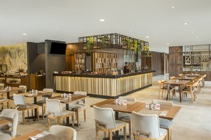 Un restaurante moderno con una zona de bar central, diversas opciones de asientos y una pared decorativa con plantas.