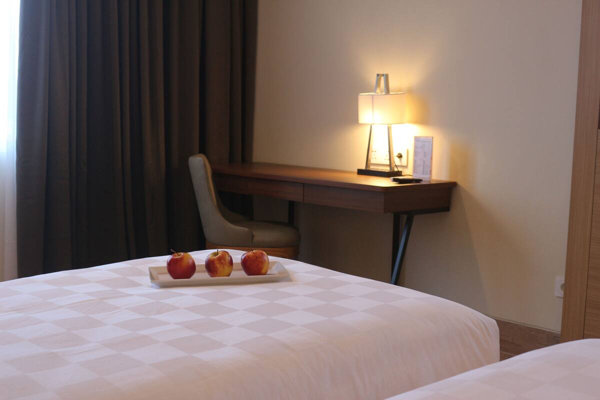 Ett hotellrum med två sängar, ett skrivbord med en lampa och en stol. Det ligger äpplen på sängen.
