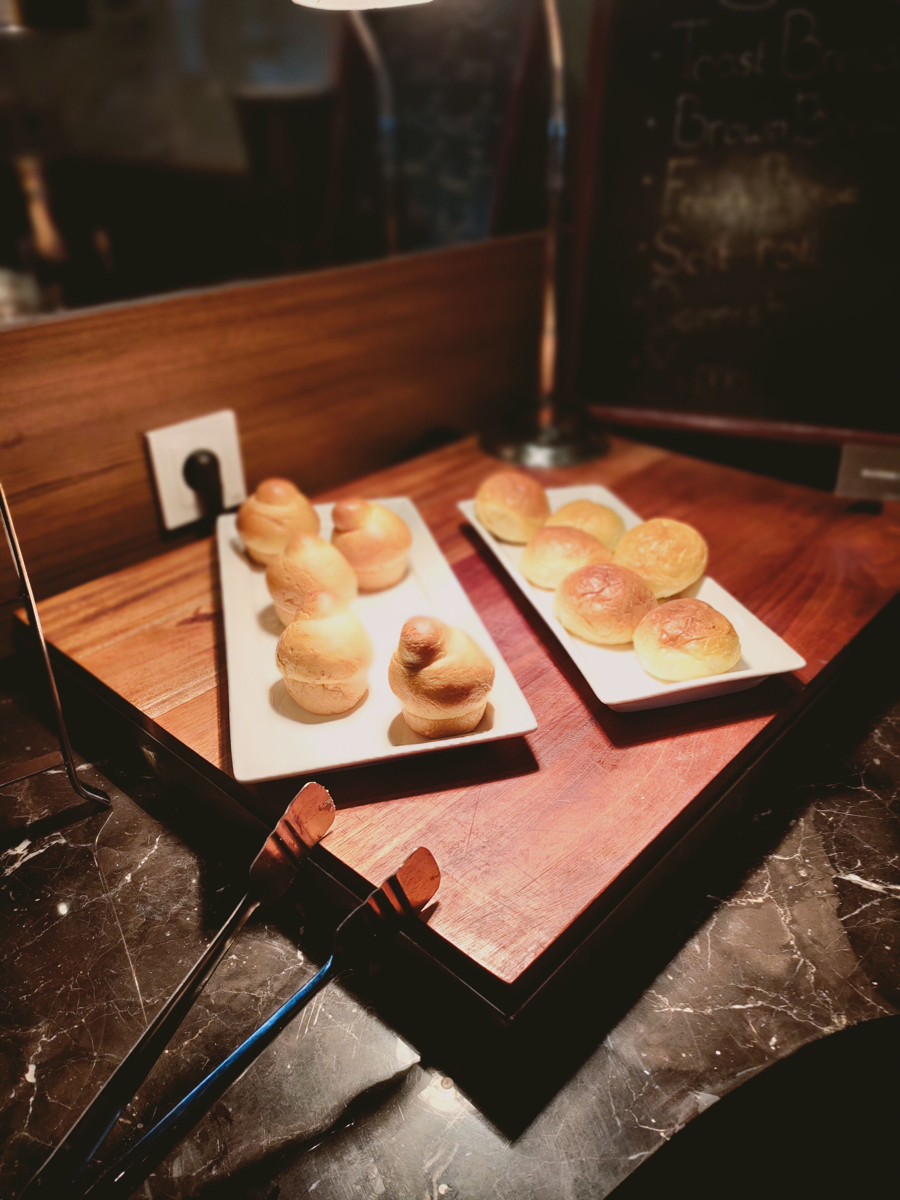 A table with two white plates of pastries, a wooden surface, and a marble countertop.