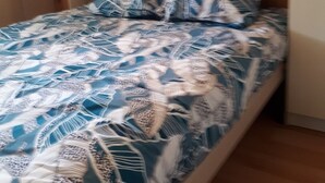 Uma cama com colcha estampada, guarda-roupa de madeira e uma faixa verde na parede.