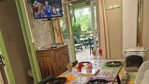 Uma área de refeições com uma mesa posta para dois, uma televisão na parede e vista para o pátio externo.