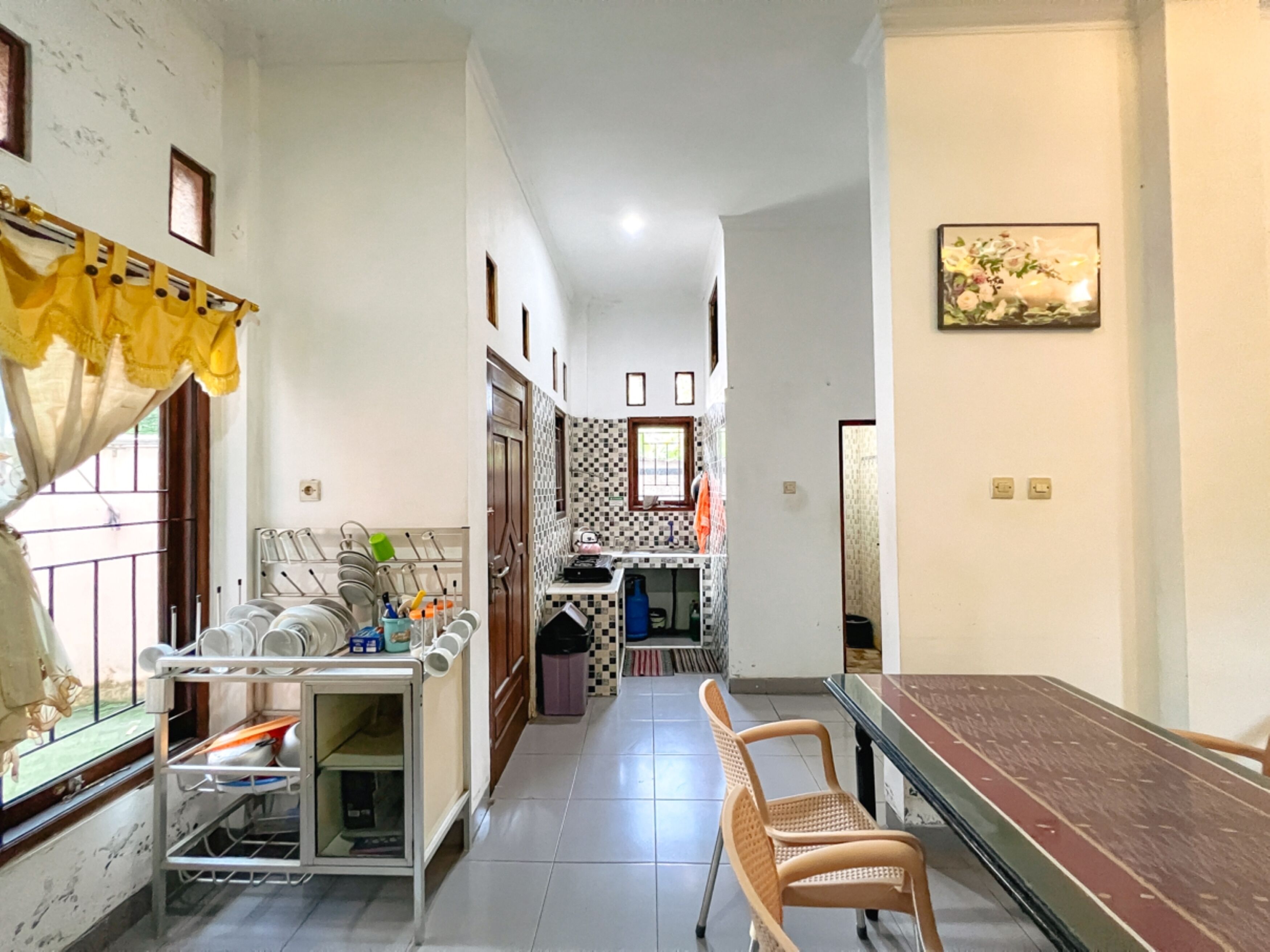 Un estrecho pasillo con una zona de comedor que incluye una mesa y sillas, una cocina con ventana y un salpicadero de azulejos.
