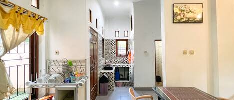 A narrow hallway with a dining area featuring a table and chairs, a kitchen area with a window, and a tiled backsplash.
