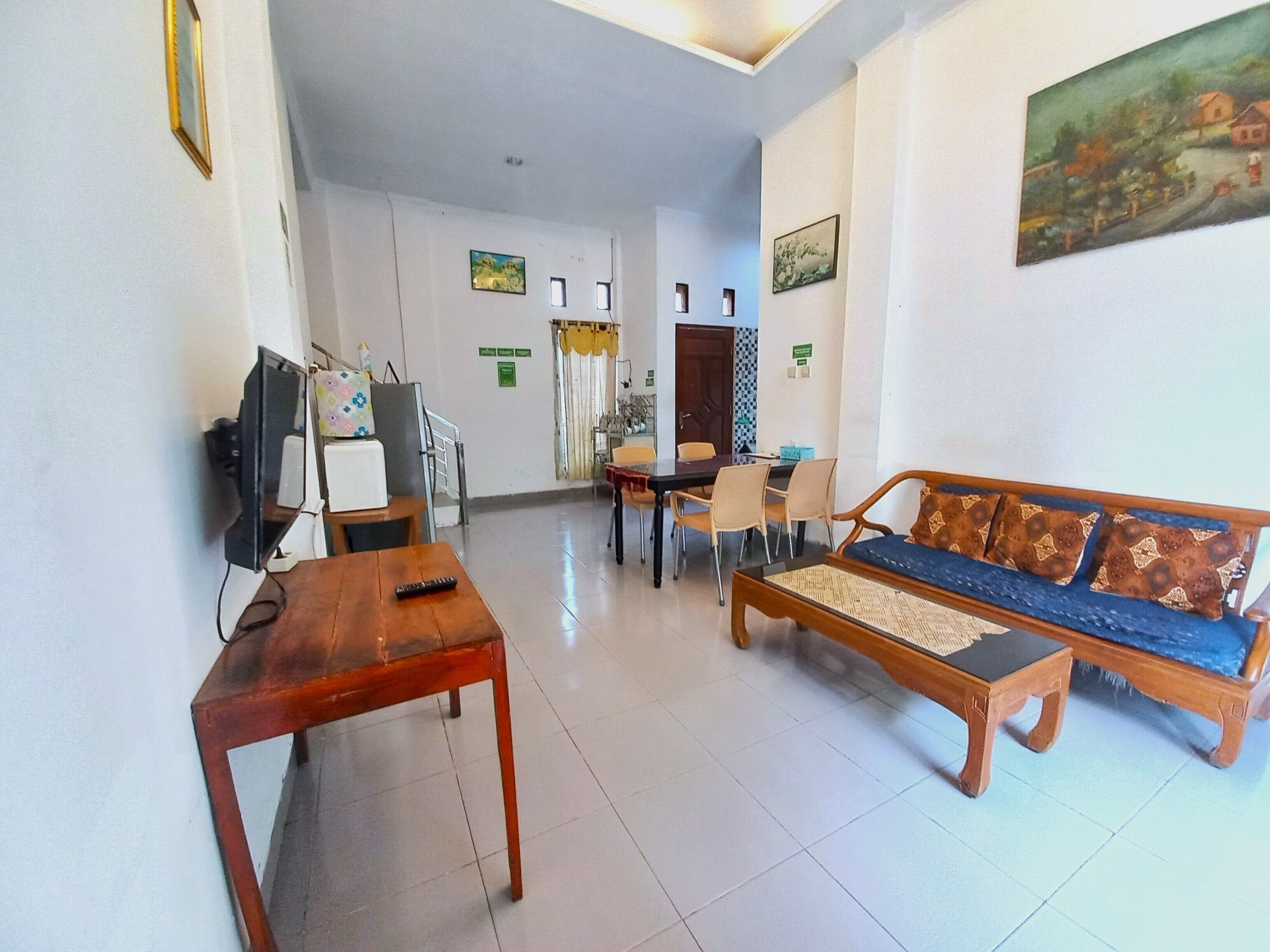 A hotel lobby with a wooden sofa, a wooden table, a television, and a small refrigerator.
