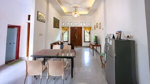 A dining area with a glass-top table and chairs, a refrigerator, and a TV on a stand. - Homestay Jogja Jakal 3 Dekat UGM by Simply Homy (Ngaglik)