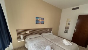 A hotel room with two beds, a painting on the wall, and a door. - KESITO FAMILY APARTAMENT BJ.-3ª (Lloret de Mar)