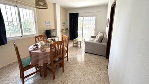 A dining area with a round table, chairs, and a hanging light fixture. There is a sofa and a TV in the background. - KESITO FAMILY APARTAMENT BJ.-3ª (Lloret de Mar)