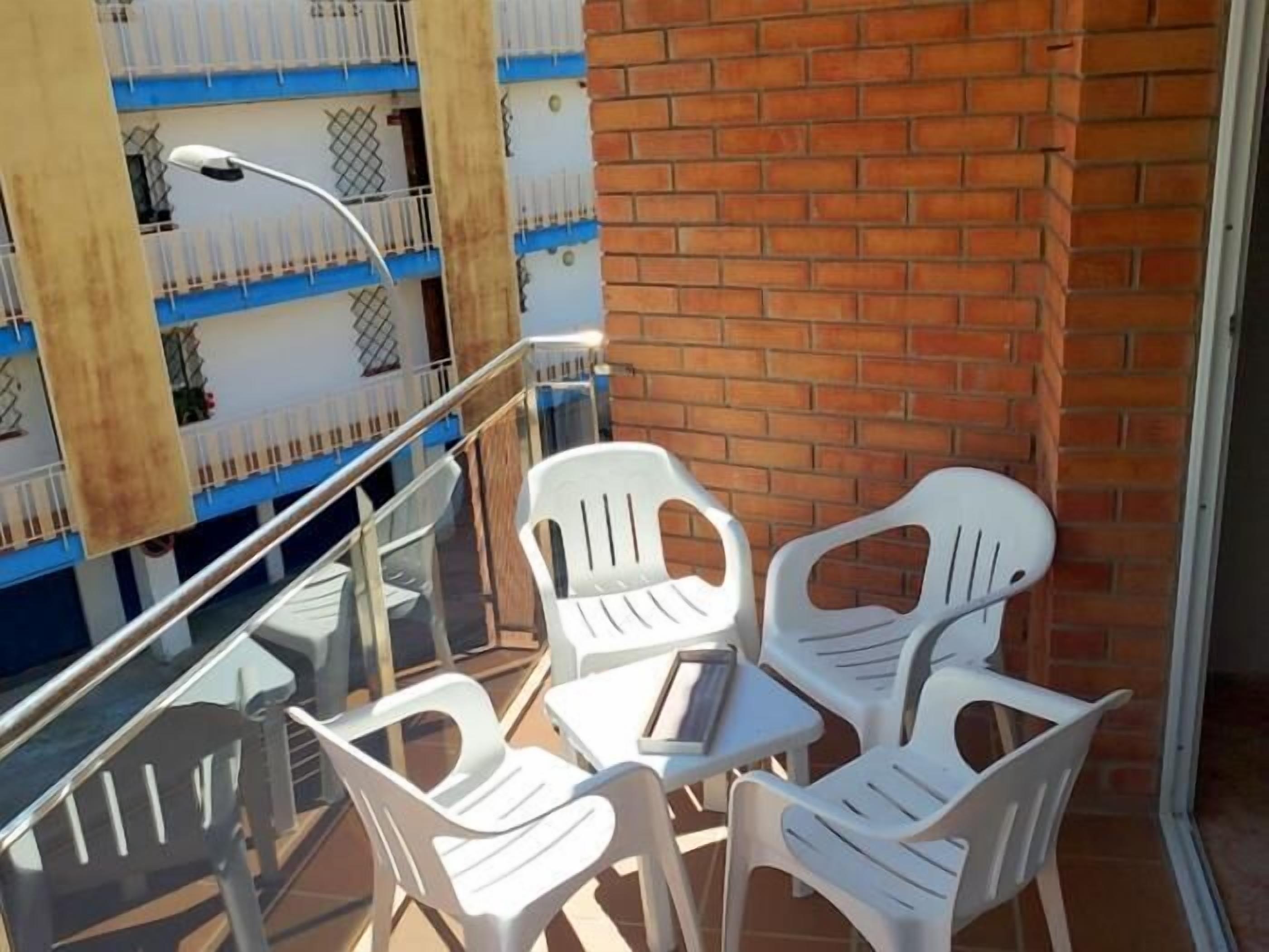 Ein Balkon mit weißen Plastikstühlen, einem kleinen Tisch, einem Metallgeländer und einer Ziegelwand.