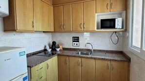 A compact kitchen with wooden cabinets, a microwave, a sink, and a refrigerator. - KESITO FAMILY APARTAMENT 1ª3ª (Lloret de Mar)