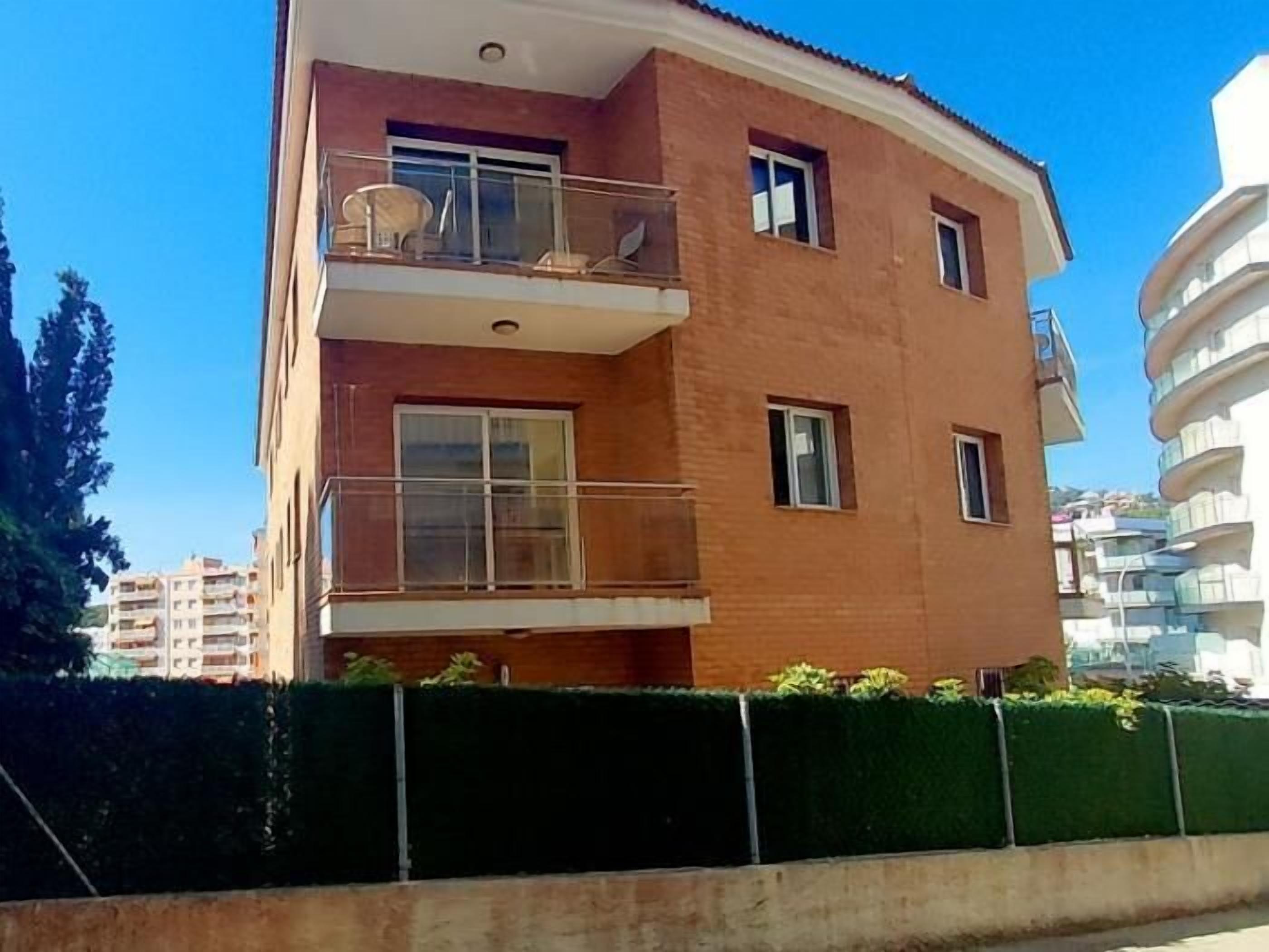 Un immeuble résidentiel à plusieurs étages, doté d’un balcon au deuxième étage, d’un toit plat et d’une haie à l’avant.
