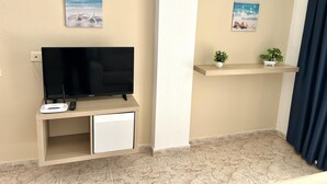 A living area with a flat-screen TV on a stand, a small cabinet below, and two wall-mounted shelves with potted plants. - KESITO FAMILY APARTAMENT 1ª3ª (Lloret de Mar)