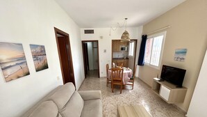 A living room with a sofa, a dining table with chairs, a TV, and artwork on the walls. - KESITO FAMILY APARTAMENT 1ª3ª (Lloret de Mar)