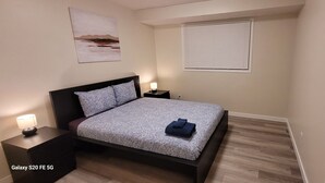 Ein Schlafzimmer mit Bett, Nachttischen, einem Fenster mit Jalousien und einer Tür.