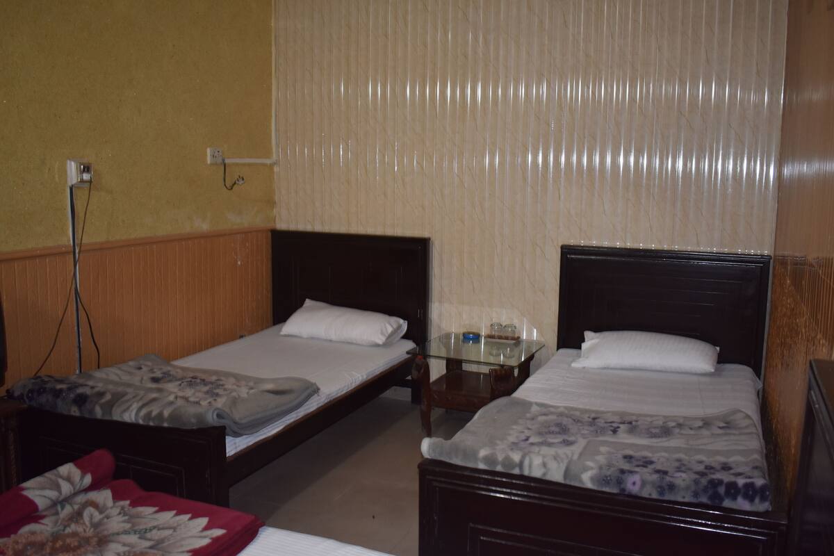 A room with two single beds, a small wooden table, and a wall-mounted electrical outlet.