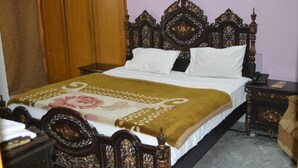 Een netjes opgemaakt bed met een bloemenprint sprei, een houten hoofdbord en een nachtkastje met een lamp.