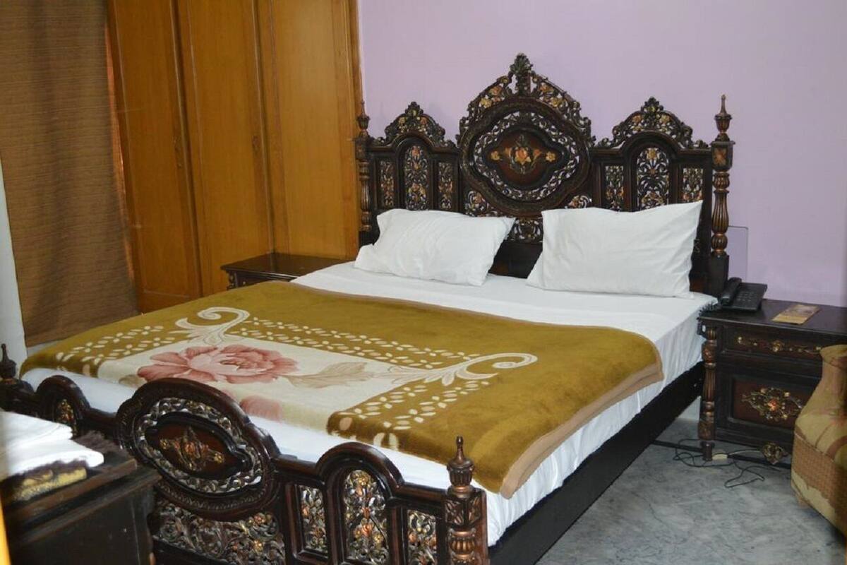 A neatly made bed with a floral bedspread, a wooden headboard, and a bedside table with a lamp.
