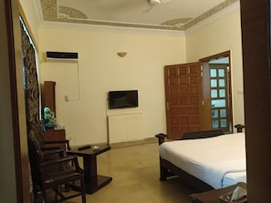 A hotel room with a bed, a TV mounted on the wall, a wooden door, and a small table with a chair. - Comfort Inn (Islamabad)