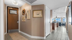 Un pasillo con puerta de madera, cuadros enmarcados, un espejo decorativo y una zona de cocina con vista al cielo.