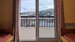 A room with a sliding glass door leading to a balcony with a view of snow-covered mountains and a wooden fence. - Cozy apartment near slopes with parking and Wifi (Le Dévoluy)