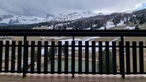 A balcony with a view of snow-covered mountains, a tennis court, and a small building. - Cozy apartment near slopes with parking and Wifi (Le Dévoluy)