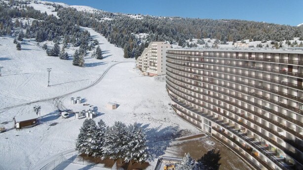 A large, multi-story hotel with a modern design, situated in a snowy mountainous area with ski slopes visible in the background. - Cozy apartment near slopes with parking and Wifi (Le Dévoluy)