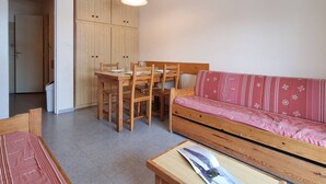 A compact living space with a dining table and chairs, a sofa, and a small table with a magazine. - Cozy apartment near slopes with parking and Wifi (Le Dévoluy)