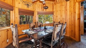 A wooden interior with a glass table, chairs with animal motifs, a ceiling fan, and windows with blinds.
