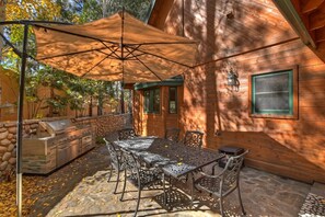 An outdoor patio with a grill, dining table, chairs, and a large umbrella. - Luxury in Boulder Bay! Hot Tub! Lake Views! Pool Table! Theater! Air Hockey! (Big Bear Lake)