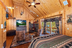 A log cabin interior with a fireplace, a television, and a bed with patterned bedding.