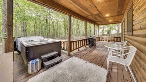 Eine Holzterrasse mit Whirlpool, Sitzgelegenheit und Blick auf den Wald.
