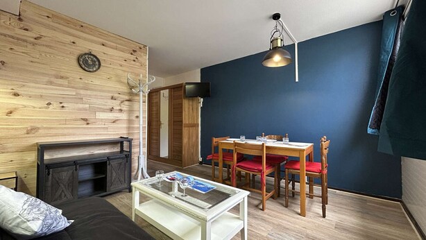 A cozy living room with a fireplace, a dining table with chairs, and a television mounted on the wall. - Studio for 4 in SuperDévoluy with Wifi (Le Dévoluy)