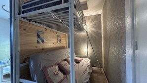 A bunk bed with a wooden headboard and a single bed below. There is a small table with a glass on it, and a wall with posters. - Studio for 4 in SuperDévoluy with Wifi (Le Dévoluy)