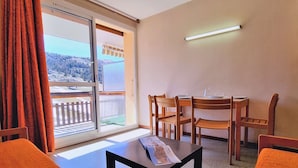 Une pièce avec une table et des chaises, une fenêtre avec des rideaux et une vue sur un paysage enneigé.