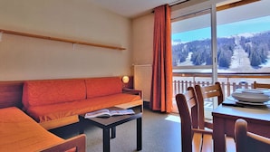 Une pièce chaleureuse avec un canapé, une petite table et une vue sur un paysage enneigé, visible à travers une grande fenêtre.