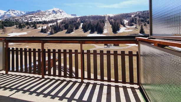 Un balcon offrant une vue sur des montagnes enneigées, une vallée boisée et un ciel dégagé.