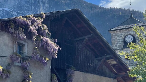 A traditional chalet with a wooden facade, a stone clock tower, and a mountain backdrop. - Family duplex in village center, pets allowed (Samoëns)
