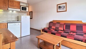Kompakti keittiö, jossa on mikroaaltouuni, jääkaappi ja astianpesukone. Keittiössä on puinen pöytä ja ruudullisella tyynyllä varustettu sohva. Seinällä on kehystetty taulu.