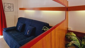 A room with a blue sofa, wooden paneling, and a red-framed mirror.
