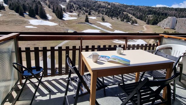 Un balcón con mesa y sillas, con vistas a un paisaje montañoso con zonas nevadas.